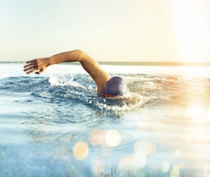 A man swimming outdoors in a pool while wearing a swimming cap. A depiction of an activity you can resume after knee replacement surgery.